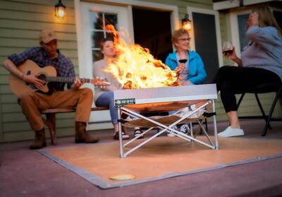 4 People gathered around the Pop-Up Fire Kit playing guitar and drinking wine